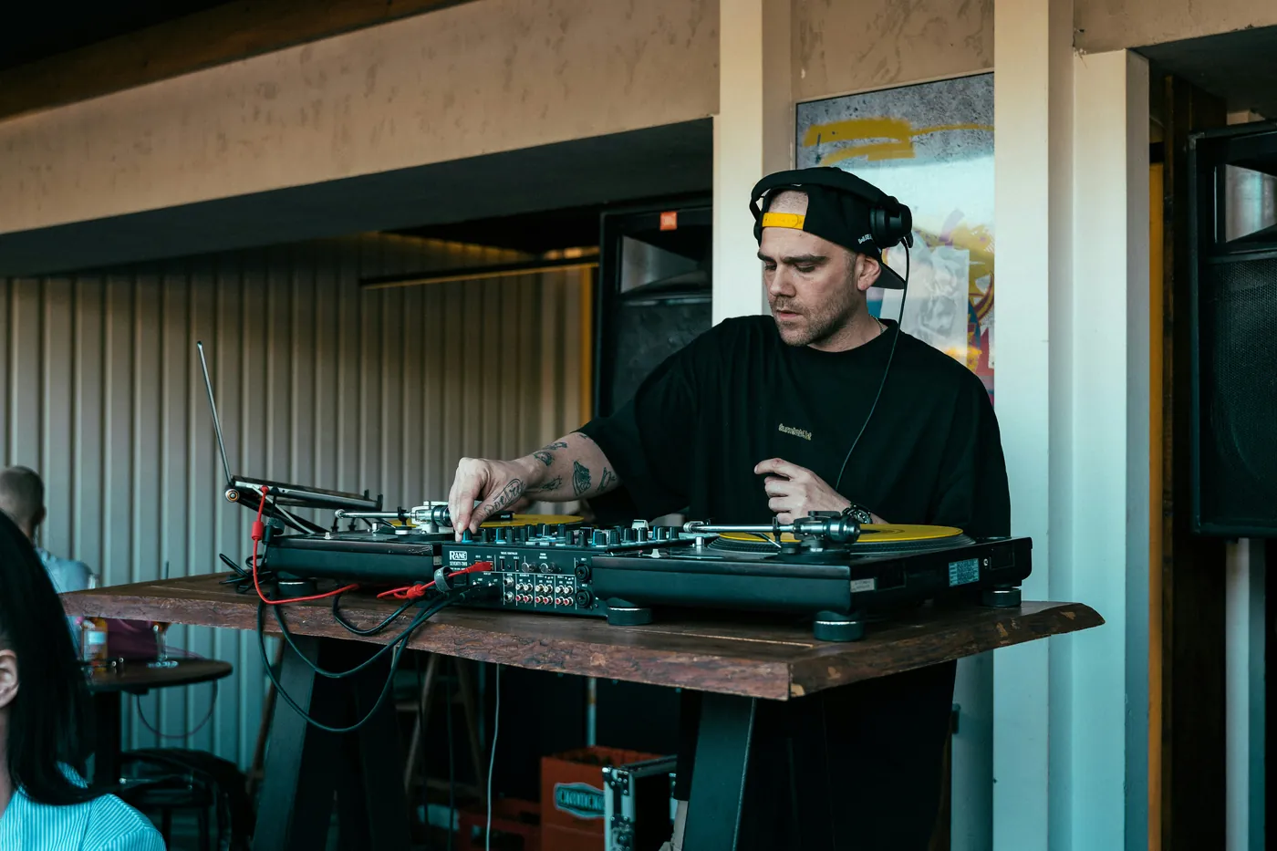 A DJ in a backwards cap mixing on turntables at a small daytime bar gig