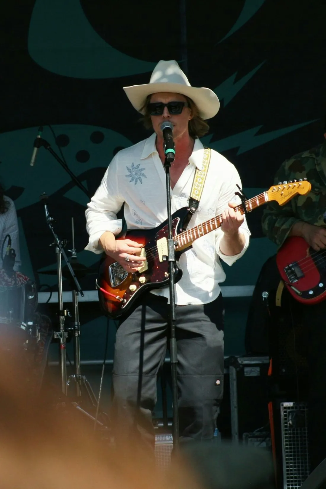 A musician singing into a mic while playing electric guitar at an outdoor festival.